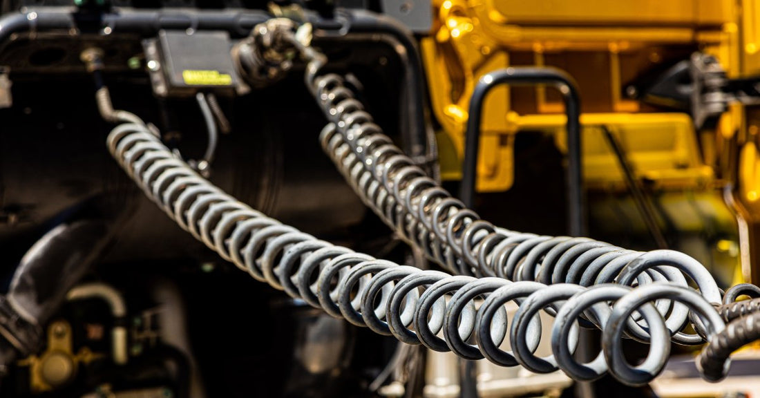 Two black, spiral hose pipes attached to the back of a semi-truck. They are stretched across the vehicle.