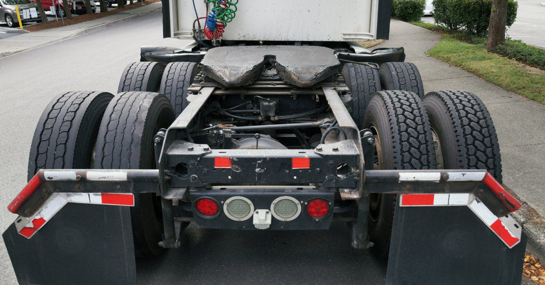The rear of a semi-truck with eight tires exposed. It is parked next to a curb near a commercial building.
