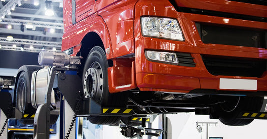 A truck with a red cab is lifted above the ground. One of its tires has been removed.