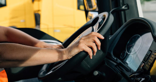 A semi-truck driver navigating through a road with both hands on the steering wheel. There is a yellow vehicle next to them.