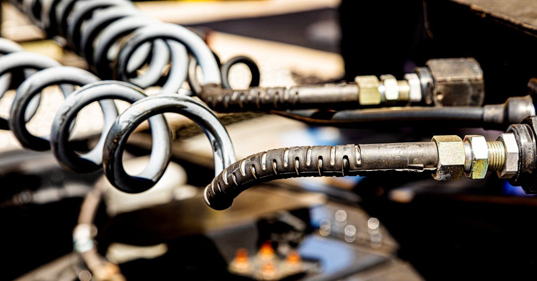 A close-up of two black spiral hose pipes attached to a semitruck. The background full of equipment is blurred.