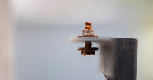 An extreme close-up of an old nut and bolt with reddish-brown rust on the surface. The background is blurred.