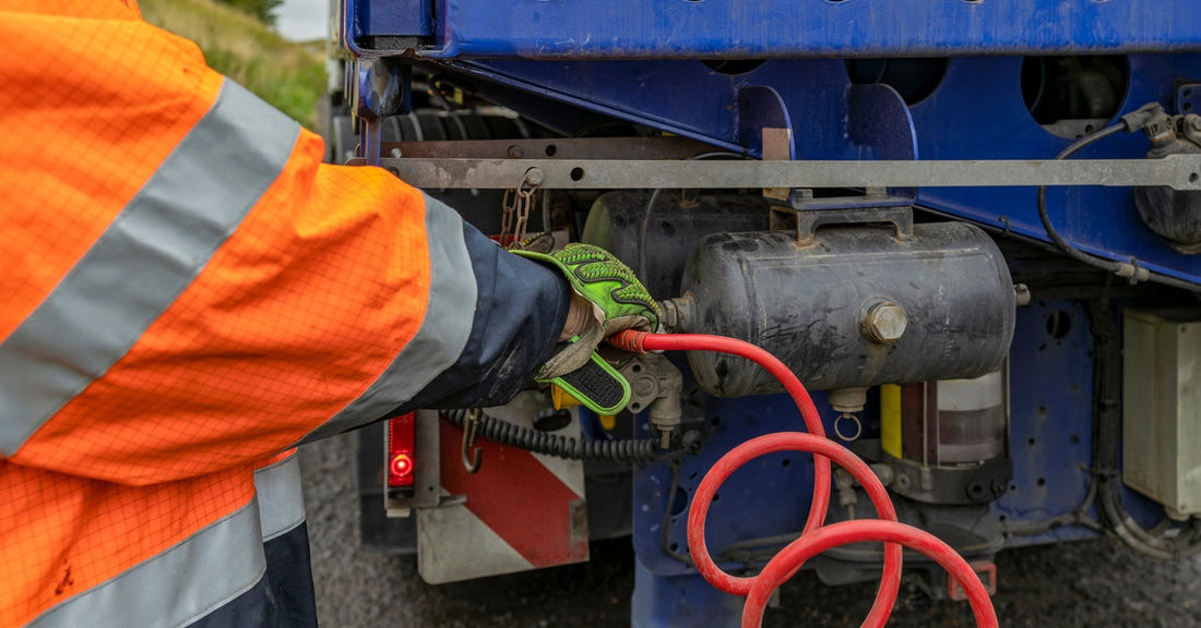 A worker wearing orange high-visibility gear connects a red coiled air hose to a blue truck's air system.