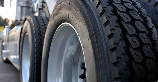 The four rear driver-side tires of a commercial trucking rig. The rest of the truck cab is visible in the background.