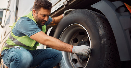 A professional mechanic checking the condition of a large truck's tires. He is looking for signs of damage and wear.