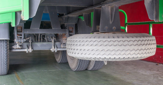 A white spare tire and wheel part for a semi-truck—the spare is mounted to the underside of the truck trailer.